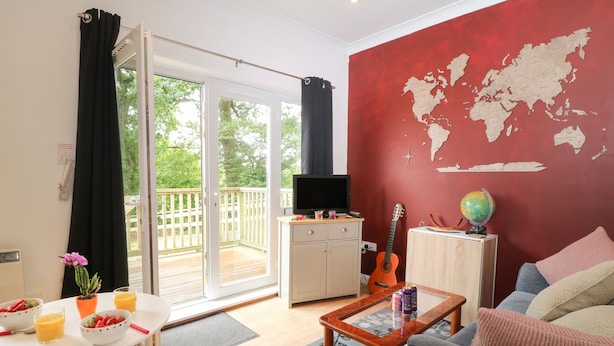 Una sala de estar con un amplio ventanal corredera que da a un balcón, un televisor, una guitarra, un globo terráqueo y un mapa del mundo en la pared.
