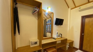 Ein gemütlicher Raum mit einem Holznähenschränkchen, einem Spiegel, einem an der Wand befestigten Fernseher, einem kleinen Kühlschrank und einer Holzbank.