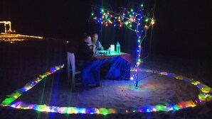 Ein Essbereich mit Tisch und Stühlen unter einer Lichterkette, auf sandigem Untergrund.