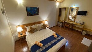 Ein Hotelzimmer mit einem hölzernen Bett, einem Schreibtisch, einem Sessel, einem Spiegel und einem Fernseher.