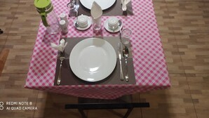 Ein Esstisch mit Geschirr, Besteck und Gläsern, bedeckt mit einer rosa-weißen karierten Tischdecke.