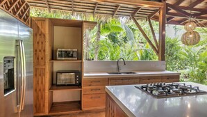 Una cocina moderna con microondas integrado, tostadora y estufa a gas, armarios de madera y un ventanal grande con vistas a un exuberante jardín.
