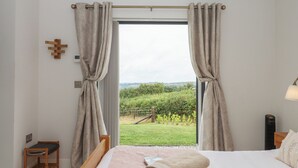 Une chambre à coucher avec un lit, une chaise en bois et une vue sur un vignoble, visible à travers une grande fenêtre ornée de rideaux.