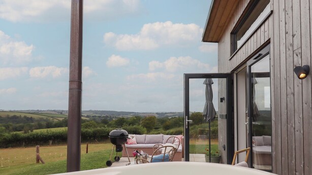 Un bain à remous avec vue sur un champ verdoyant et un bâtiment en bois doté d’une porte en verre.