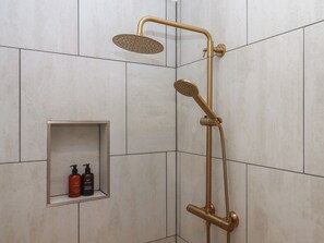 A shower with a gold-colored showerhead and hose, mounted on a tiled wall. - The Bickleigh (Tiverton)