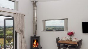 Une pièce moderne dotée d’un poêle à bois, d’une table à manger avec des chaises, d’une fenêtre offrant une vue agréable et d’une porte donnant sur un espace extérieur.