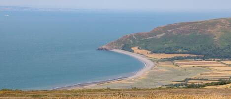A coastal landscape with a beach, fields, and hills.