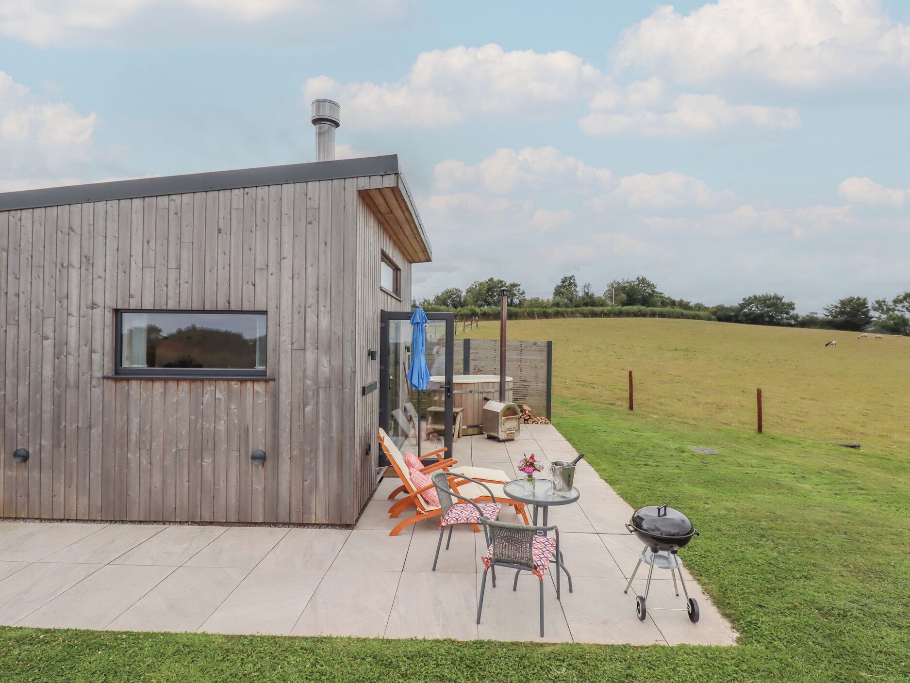 Ein modernes Holzhaus mit einer Terrassenfläche, die Gartenmöbel, einen Grill und einen Holzofen zeigt.