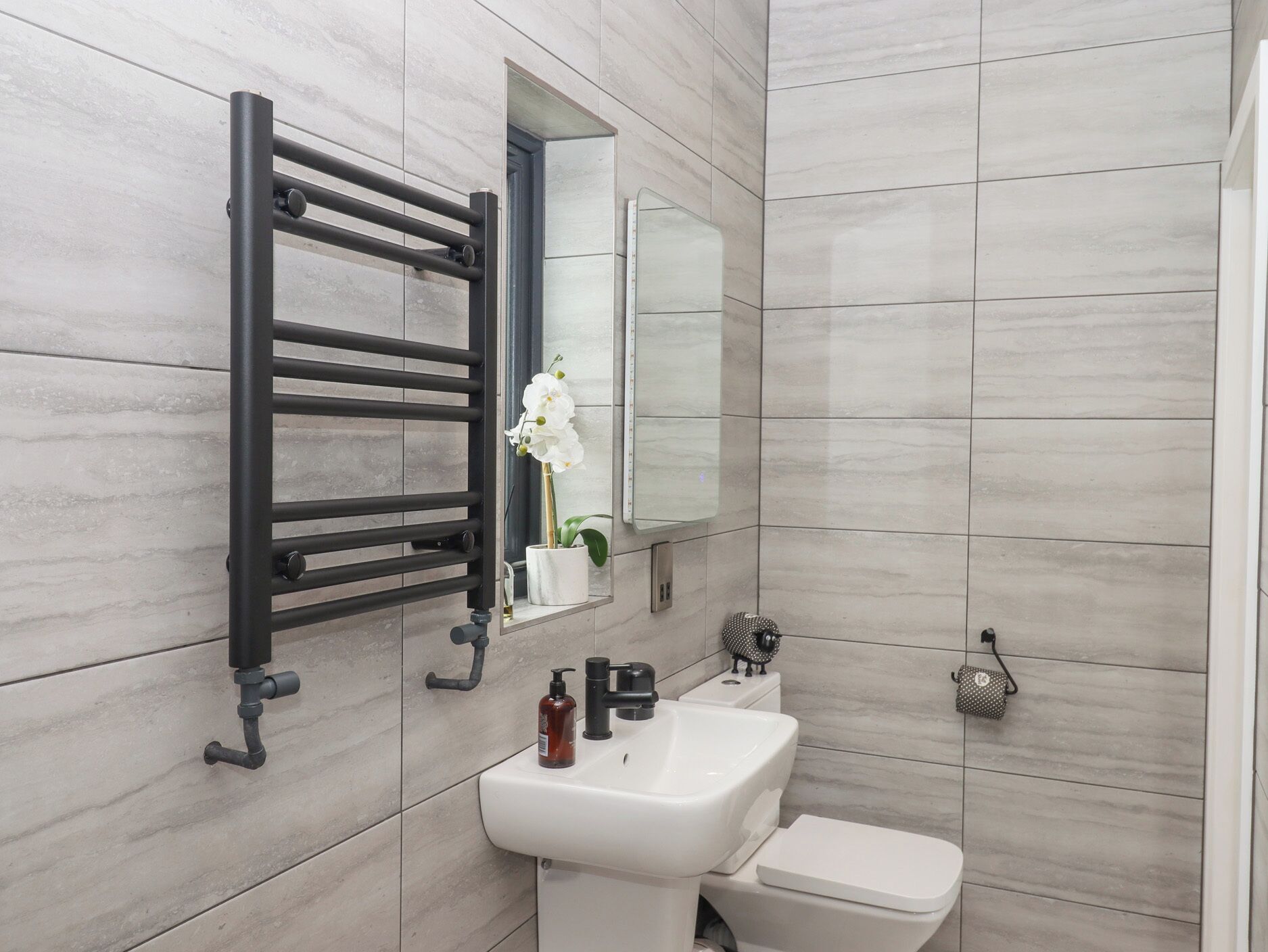 A modern bathroom with a white sink, a toilet, and a black towel rack.