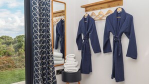 A bathroom with a large mirror, wooden towel rack, and three blue robes hanging on the wall. - The Cadeleigh (Tiverton)