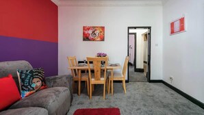 Ein Zimmer mit Esstisch gedeckt für vier Personen, ein graues Sofa mit rotem Kissen und einem roten Teppich.