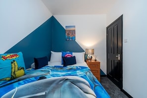 A bedroom with a bed, pillows, a nightstand, a lamp, and a door.