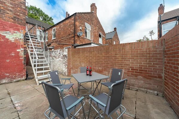 A patio with a table and chairs, a ladder, and a brick wall.
