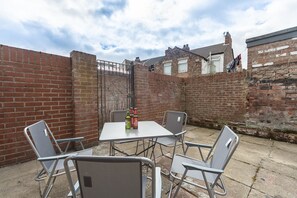 Ein Patio mit Tisch und Stühlen, einer Ziegelwand und einem Tor.