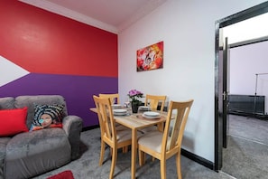 A dining area with a table set for four, a sofa with a colorful cushion, and a wall with a musical note painting.
