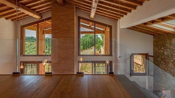 Ein geräumiges Zimmer mit Holzböden, großen Fenstern mit Blick auf einen Wald und einer Steinwand.