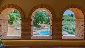 Blick durch drei Ziegelbögen auf einen Pool und Bäume.