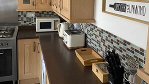 Eine moderne Küche mit Holzausstattung, einer Mikrowelle, einem Toaster und einer Spritzschutzleiste mit dem Schriftzug 'Uncork and Unwind'.