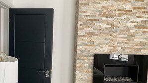 Ein Zimmer mit einer schwarzen Tür, einer Steinwand mit eingebautem Kamin und einem kleinen Tisch mit einer Lampe.