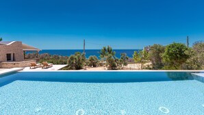 A clear blue pool with lounge chairs, a stone building, and a view of the sea. - Villa Lodrea by Perle di Puglia (Torre Vado)