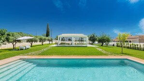 Una piscina con cerramiento de vidrio, rodeada de césped cuidado y árboles.