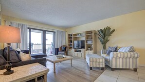 Een woonkamer met een bank, fauteuil, salontafel, tv-meubel en een grote plant.