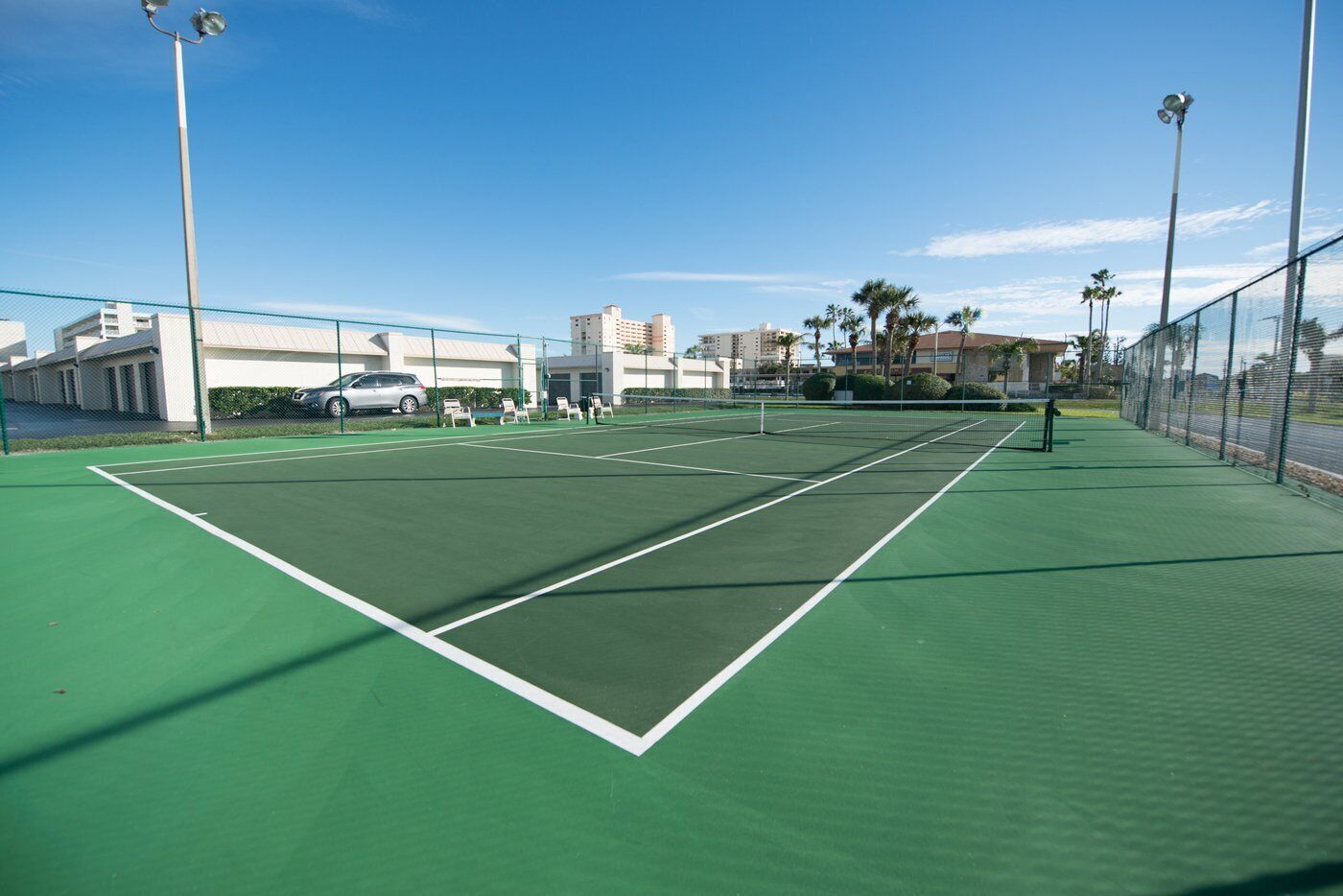 Un court de tennis avec un filet, entouré d’une clôture, et des bâtiments en arrière-plan.