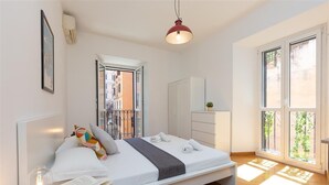 Une chambre moderne avec un lit, une table de chevet et une fenêtre donnant sur des immeubles.