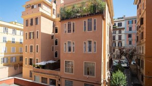 Un immeuble à plusieurs étages doté de balcons, d’un petit espace extérieur aménagé en coin salon et donnant sur une rue étroite.