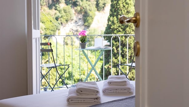 Ein Balkon mit Blick auf eine gebirgige Landschaft, ein Tisch mit einer Topfpflanze und ordentlich gefaltete Handtücher auf einem Bett.