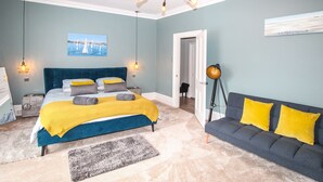 Ein Schlafzimmer mit einem Bett, einem Schlafsofa, einer Stehlampe, einem Gemälde und einer Tür zu einem anderen Raum.