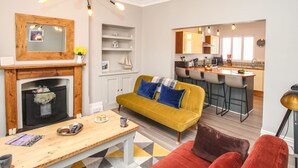 Ein modernes Wohnzimmer mit einem gelben Sofa, einem Kamin und einer Essecke mit Bar.