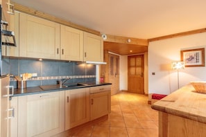 Une cuisine avec des meubles de rangement en bois, un évier et un plan de travail. Une porte donne accès à une autre pièce.