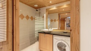 A compact bathroom with a glass shower enclosure, a sink, a washing machine, and wooden cabinets. - 50m from ski slopes, floor -2, view valley, swimming pool, balcony, tv, ski locker, 76m², Les Arcs (Bourg-Saint-Maurice)