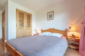Quarto com cama de madeira, duas mesas de cabeceira com luminárias, guarda-roupa de madeira e um quadro na parede.