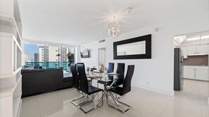 A modern dining area with a glass table and chairs, a black-framed mirror on the wall, and a city view through large windows. - Wake up over the Atlantic | Private beach access, pool & gym (Hollywood)