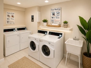 A laundry room with two front-loading washers and dryers, a sink, and a potted plant.
