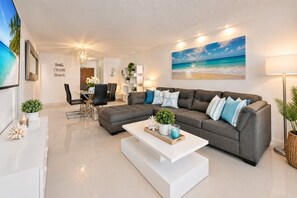 A modern living room with a sectional sofa, a coffee table, and a dining area with chairs. - Wake up over the Atlantic | Private beach access, pool & gym (Hollywood)