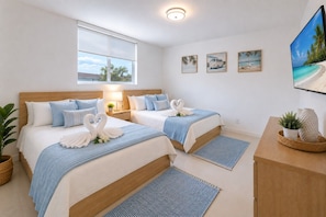 A hotel room with two beds, a large window, a flat-screen TV, and a wall with three framed pictures.