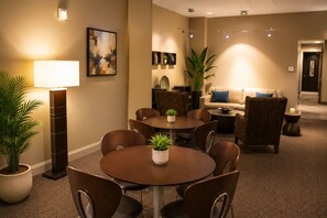 A hotel room with a dining area, a sofa, a lamp, and a painting on the wall.