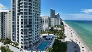 A high-rise hotel with a pool and beach view, surrounded by palm trees and other buildings. - Wake up over the Atlantic | Private beach access, pool & gym (Hollywood)