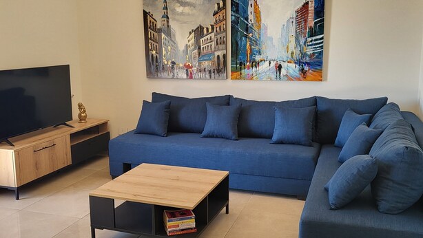A living room with a blue sofa, a coffee table, a TV, and two paintings on the wall. - Sweet Home Apartment (Batroun)