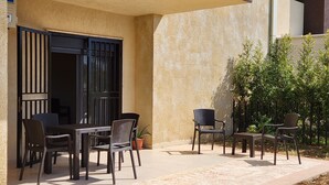 An outdoor patio area with a table and chairs, a potted plant, and a wall with a textured surface. - Sweet Home Apartment (Batroun)