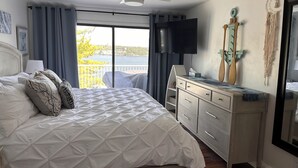 Un dormitorio con cama, cómoda, televisor y balcón con vistas.