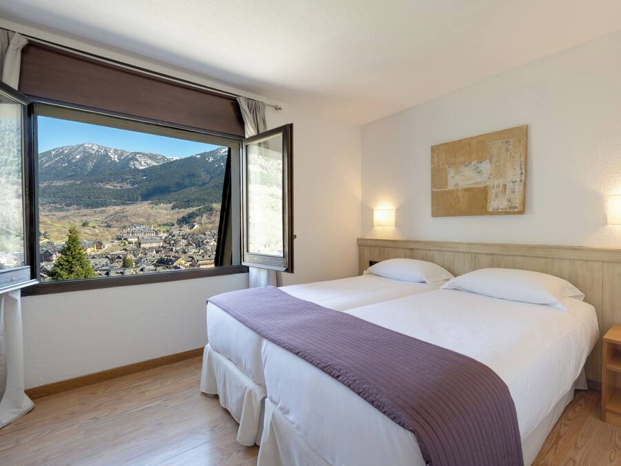 Een slaapkamer met twee bedden, een groot raam met uitzicht op de bergen en een schilderij aan de muur.