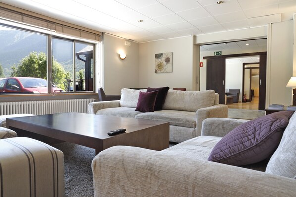 A modern hotel lobby with a sofa set, a coffee table, and a large window offering a mountain view.