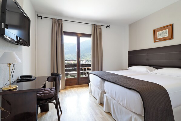 Una habitación de hotel con una cama, un escritorio con lámpara, una silla y un televisor montado en la pared.