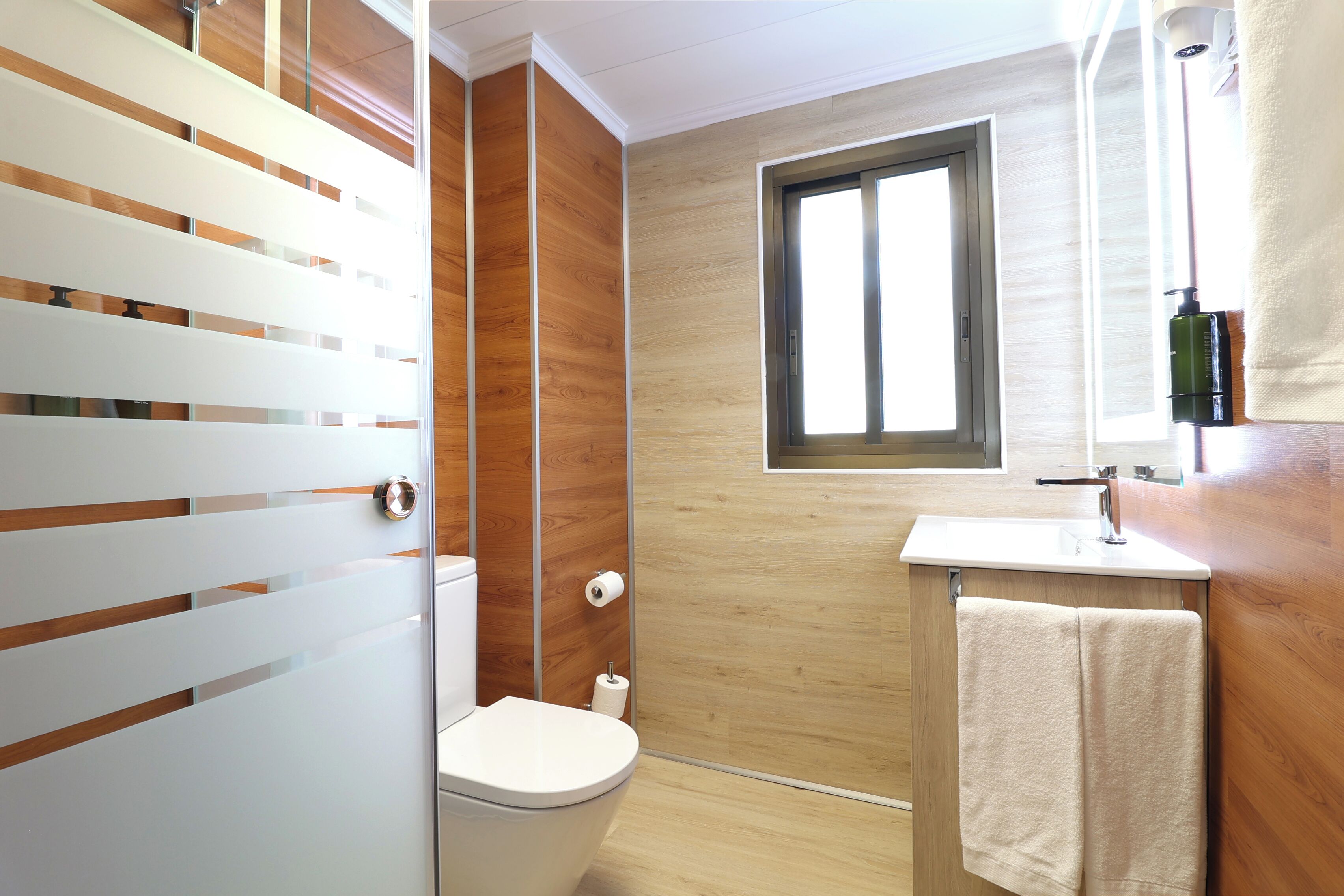 Een moderne badkamer met een houten wand, een toilet, een wastafel en een raam.