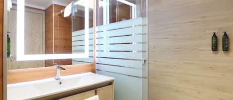 A modern bathroom with a wooden vanity, a large mirror, and a glass shower enclosure.