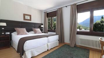 A bedroom with a bed, nightstands, a window with curtains, a radiator, and a framed picture on the wall.